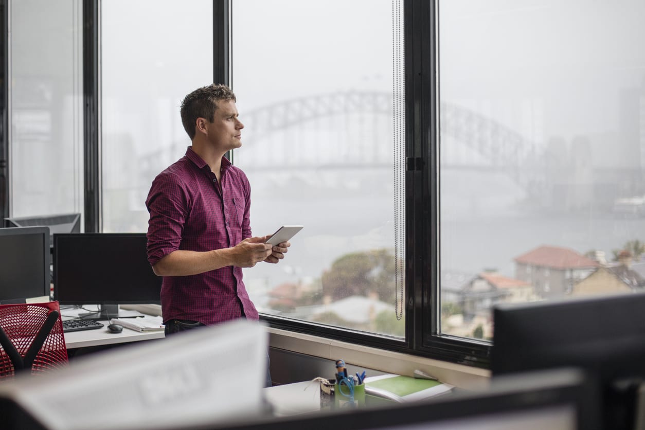 Businessman using tablet computer in office Businessman using tablet computer in office, he's looking through the window with the Sydney harbour bridge in the background.
