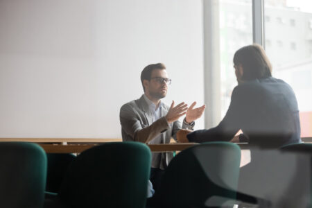 Focused confident young businessman in eyewear explaining project details to concentrated male client. Serious hr manager listening to skilled job applicant self presentation at interview in office.
