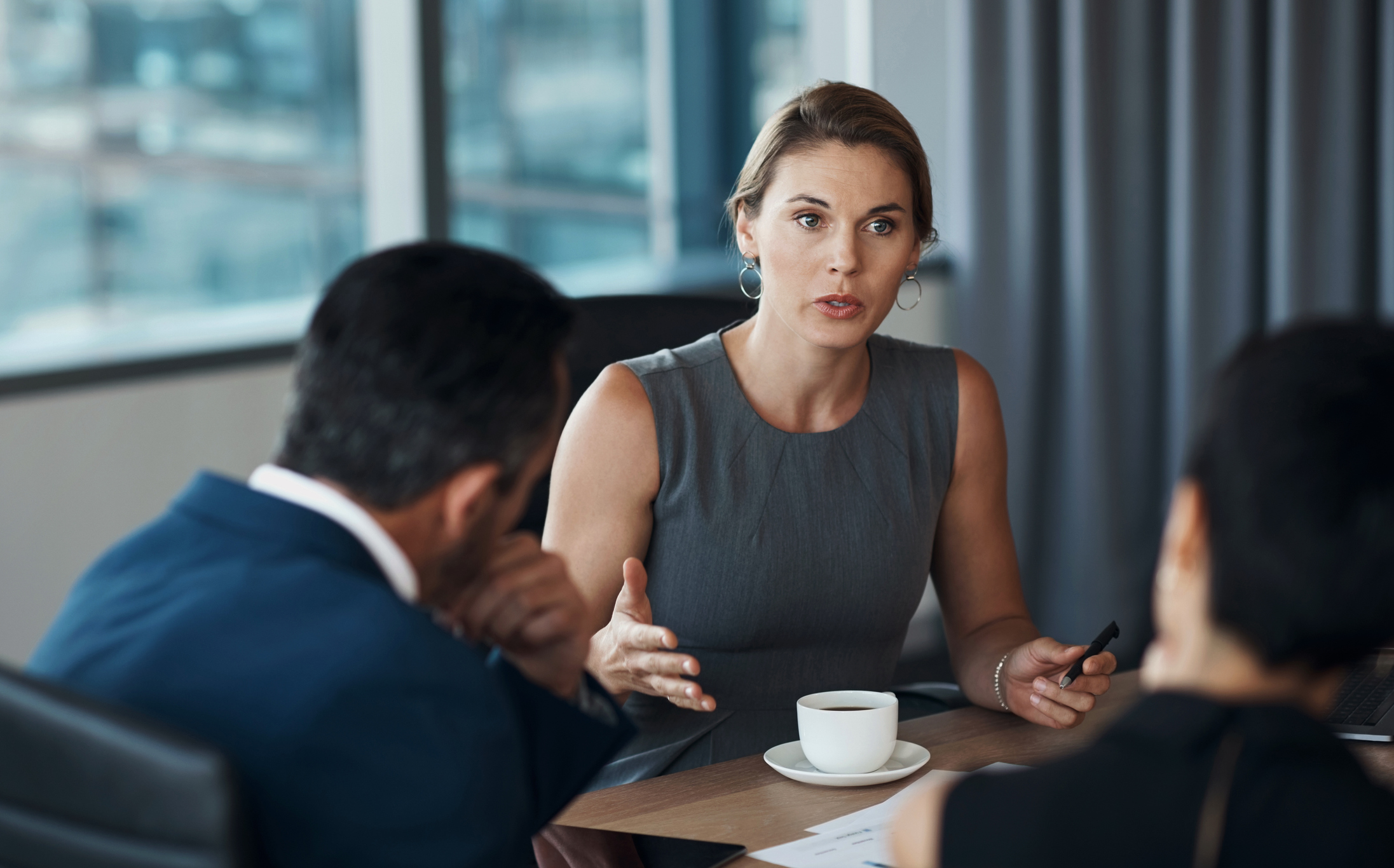 A group of professionals engaged in a serious discussion around a table with a coffee cup in a modern office setting.